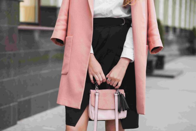 
					young stylish beautiful woman walking in street, wearing pink coat, holding purse, black skirt, fashion outfit, autumn trend, accessories, hands close-up, details